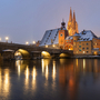 Steinbrücke und Altstadt im Winter mit beleuchtetem Kirchturm im Hintergrund Regensburg