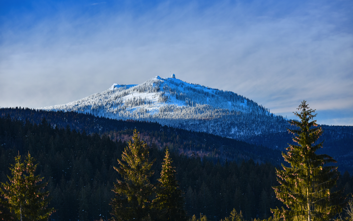 Schneebedeckter Berg mit Nadelwald im Vordergrund unter blauem Himmel Großer Arber im Bayerischen Wald