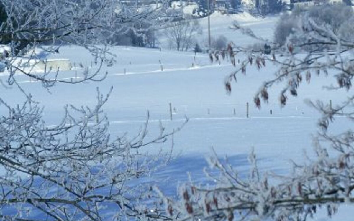 Verschneite Ortsansicht mit Kirche und umliegender Landschaft im Winter.