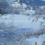 Verschneite Ortsansicht mit Kirche und umliegender Landschaft im Winter.