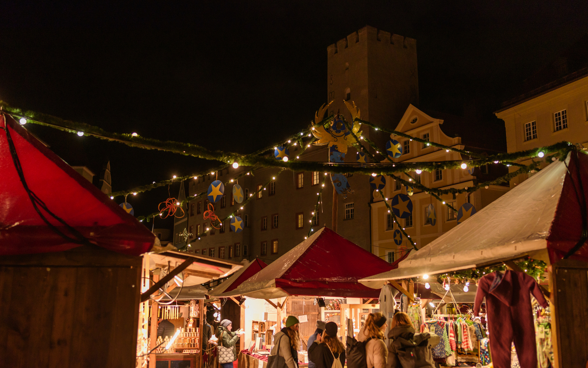 Weihnachtsmarktstände bei Nacht mit Lichtern und Besuchern. Lukrezia Weihnachtsmarkt Regensburg