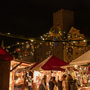 Weihnachtsmarktstände bei Nacht mit Lichtern und Besuchern. Lukrezia Weihnachtsmarkt Regensburg