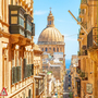 Straße in Valletta mit Blick auf eine Kuppel und das Meer im Hintergrund.