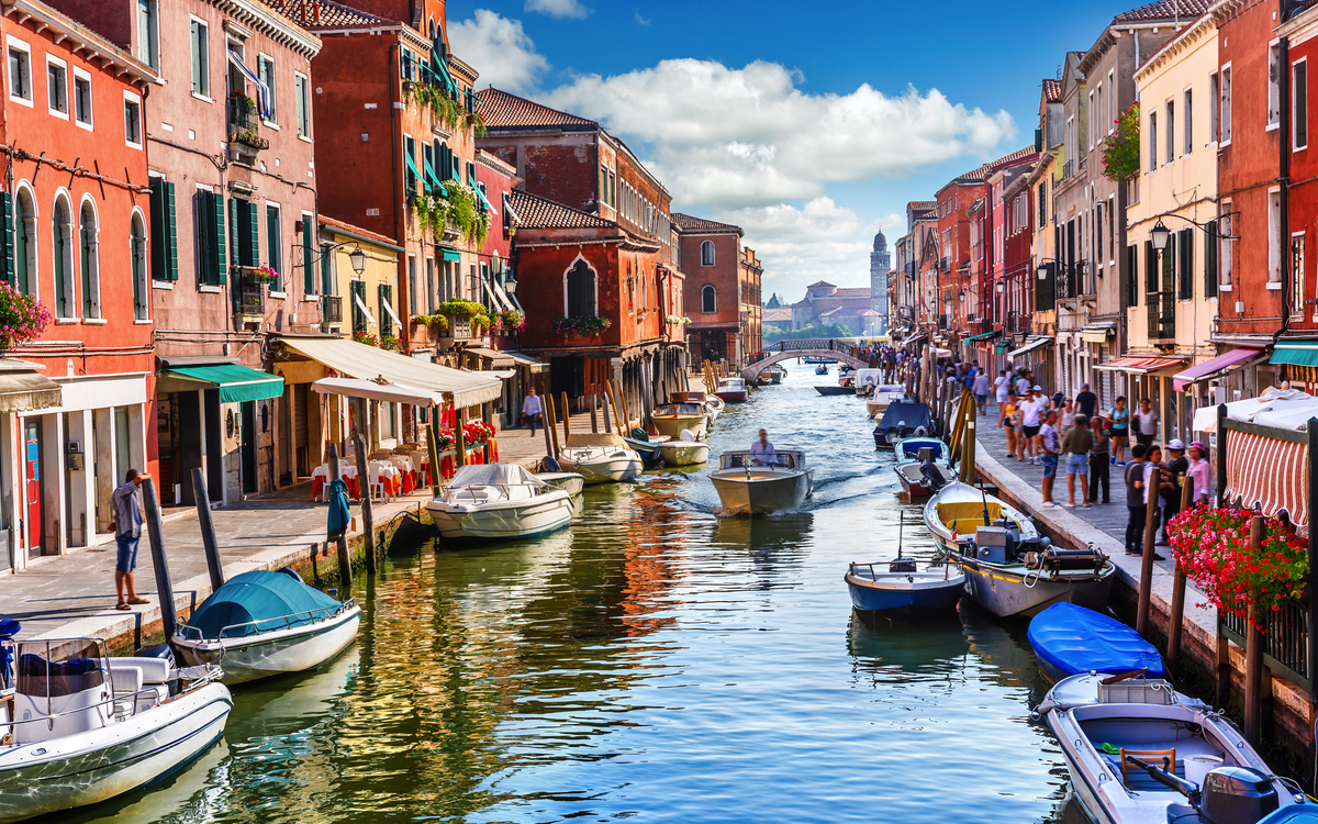 Kanal in Murano mit Booten und bunten Häusern bei Tag.