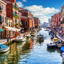 Kanal in Murano mit Booten und bunten Häusern bei Tag.