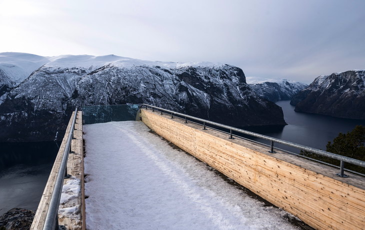 Schneegepfad mit Aussicht auf verschneite Berge und einen tiefen Fjord.