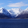 Verschneite Berge am Rand eines ruhigen Sees unter blauem Himmel.