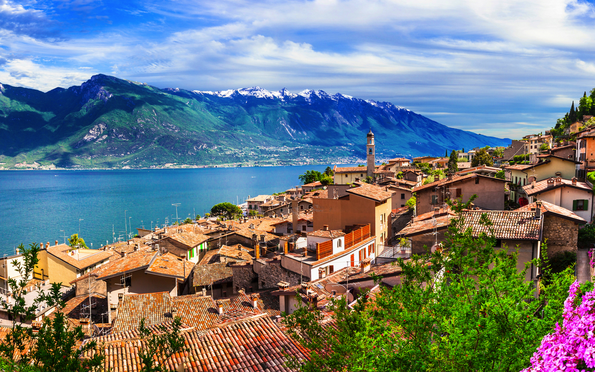 Panoramablick auf Limone sul Garda am Gardasee mit malerischen Häusern und bunten Blumen im Vordergrund, umgeben von Bergen und dem blauen Wasser des Sees.