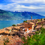 Panoramablick auf Limone sul Garda am Gardasee mit malerischen Häusern und bunten Blumen im Vordergrund, umgeben von Bergen und dem blauen Wasser des Sees.