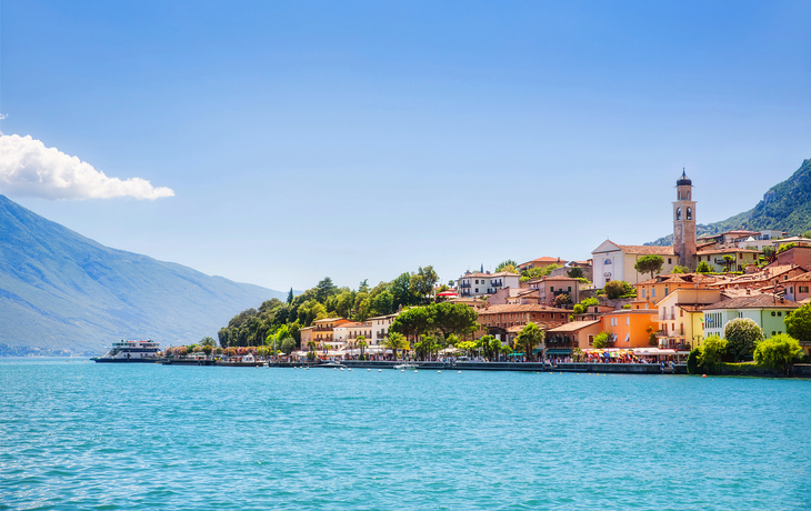Blick auf die Stadt Limone sul Garda am Gardasee in Italien mit türkisfarbenem Wasser im Vordergrund und historischen Gebäuden im Hintergrund.