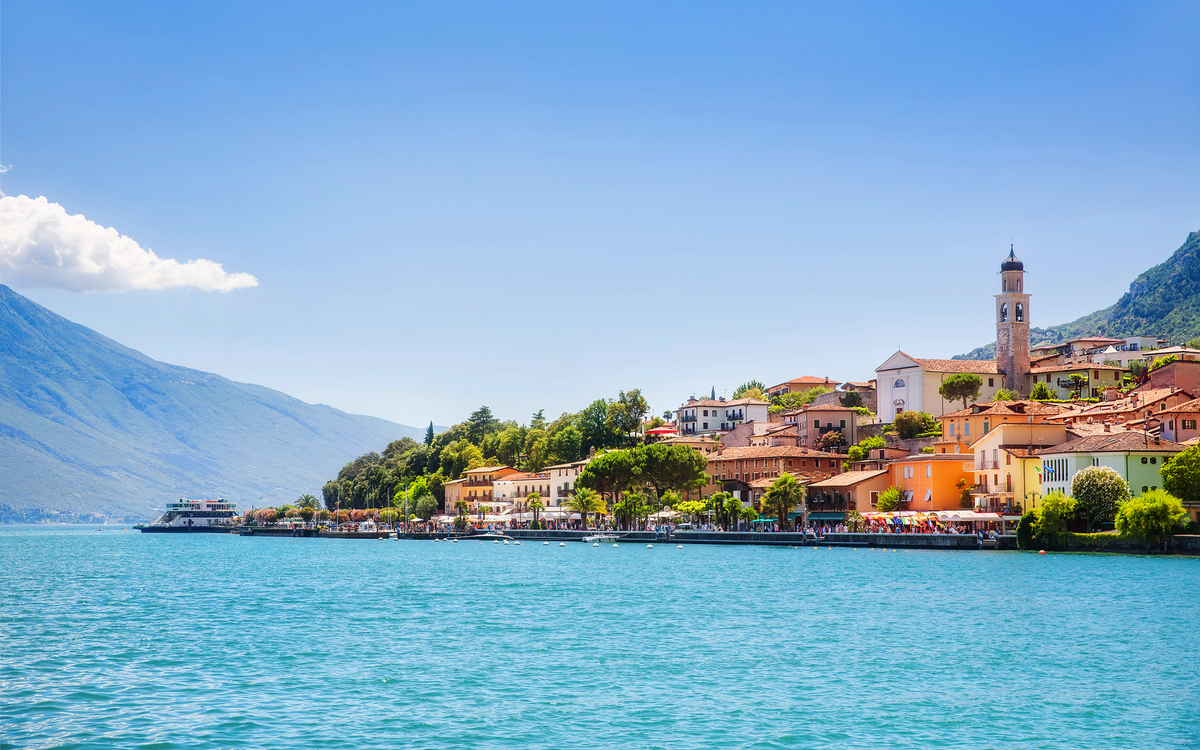 Blick auf die Stadt Limone sul Garda am Gardasee in Italien mit türkisfarbenem Wasser im Vordergrund und historischen Gebäuden im Hintergrund.