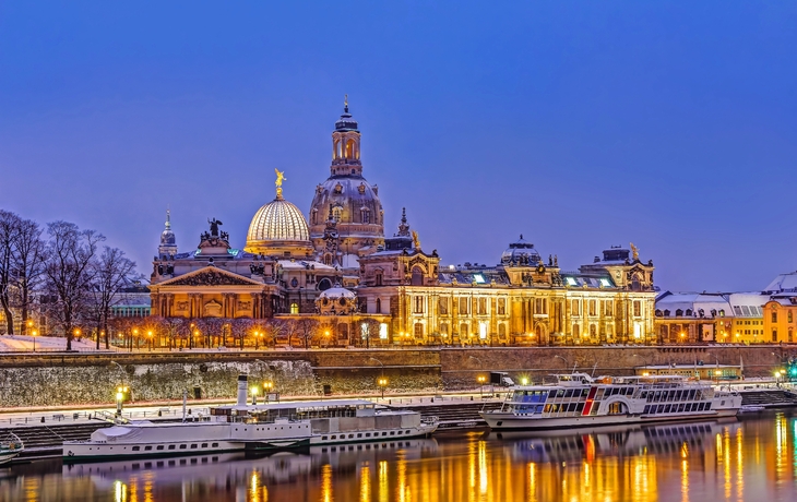 Beleuchtete historische Gebäude am Ufer eines Flusses bei Abenddämmerung.