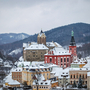 Loket Verschneite Stadt mit Kirche und Burg vor bewaldeten Hügeln im Hintergrund.