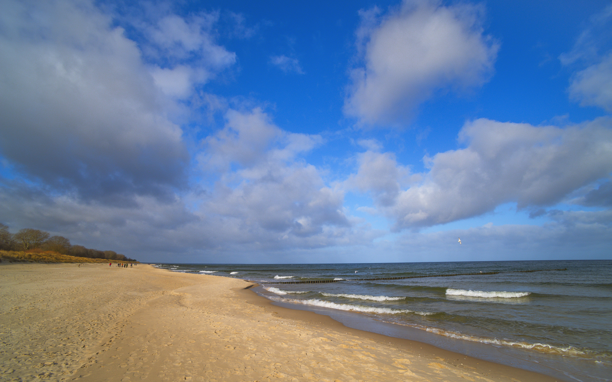 Sandstrand unter blauem Himmel mit Wolken und Wellen im Meer.
