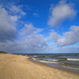 Sandstrand unter blauem Himmel mit Wolken und Wellen im Meer.