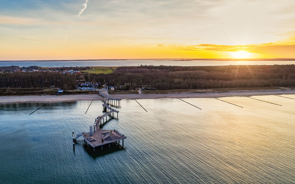 Seebrücke über ruhiges Meer bei Sonnenuntergang, Wald und Küste im Hintergrund. Koserow