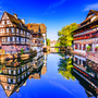 Fachwerkhäuser an einem Flussufer, spiegeln sich im Wasser, blauer Himmel.
