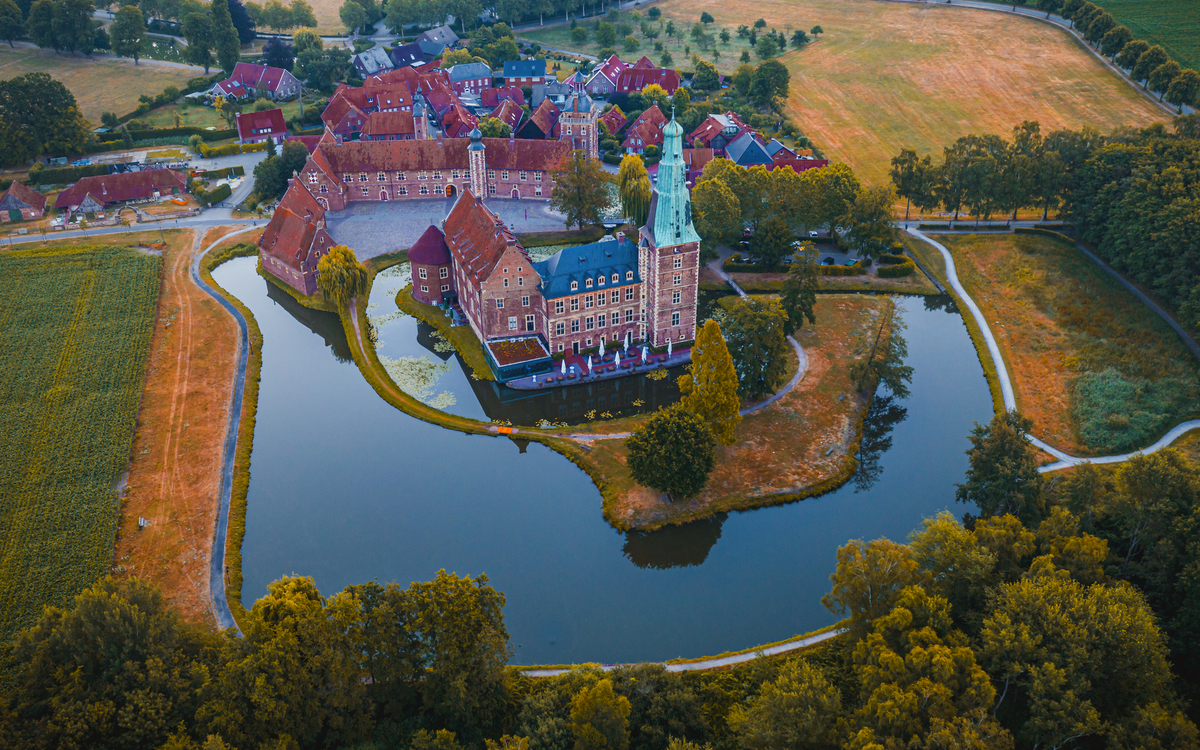Luftaufnahme einer mittelalterlichen Burg mit Wassergraben und umliegender Landschaft.