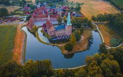Luftaufnahme einer mittelalterlichen Burg mit Wassergraben und umliegender Landschaft.