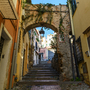 Treppenstraße mit steinernem Bogen und überwachsenen Pflanzen in einer Altstadt. Sanremo