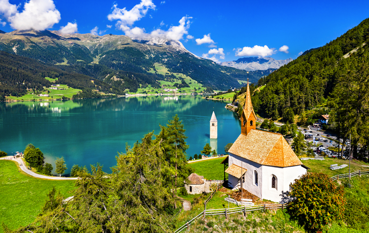 Kirche und halbversunkener Kirchturm an einem See in den Alpen.