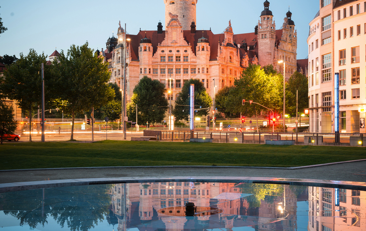 Altes Rathaus in Leipzig bei Abenddämmerung mit Spiegelung im Wasser im Vordergrund.