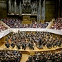 Ein Orchester spielt vor einem großen Publikum in einem Konzertsaal.