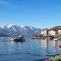 Stadt am See mit Bergen im Hintergrund und Blumen im Vordergrund.