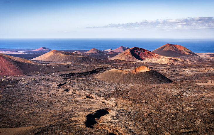 Vulkankrater in einer kargen, steinigen Landschaft mit Blick auf das Meer am Horizont
