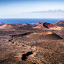 Vulkankrater in einer kargen, steinigen Landschaft mit Blick auf das Meer am Horizont