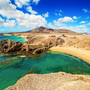 Küste mit blauem Meer und Sandstrand, Hügel im Hintergrund.