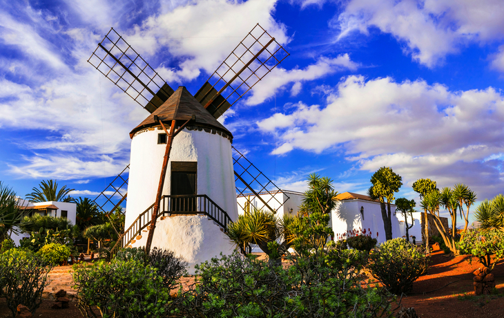 Traditionelle Windmühle in einer Landschaft mit blauem Himmel und Wolken.