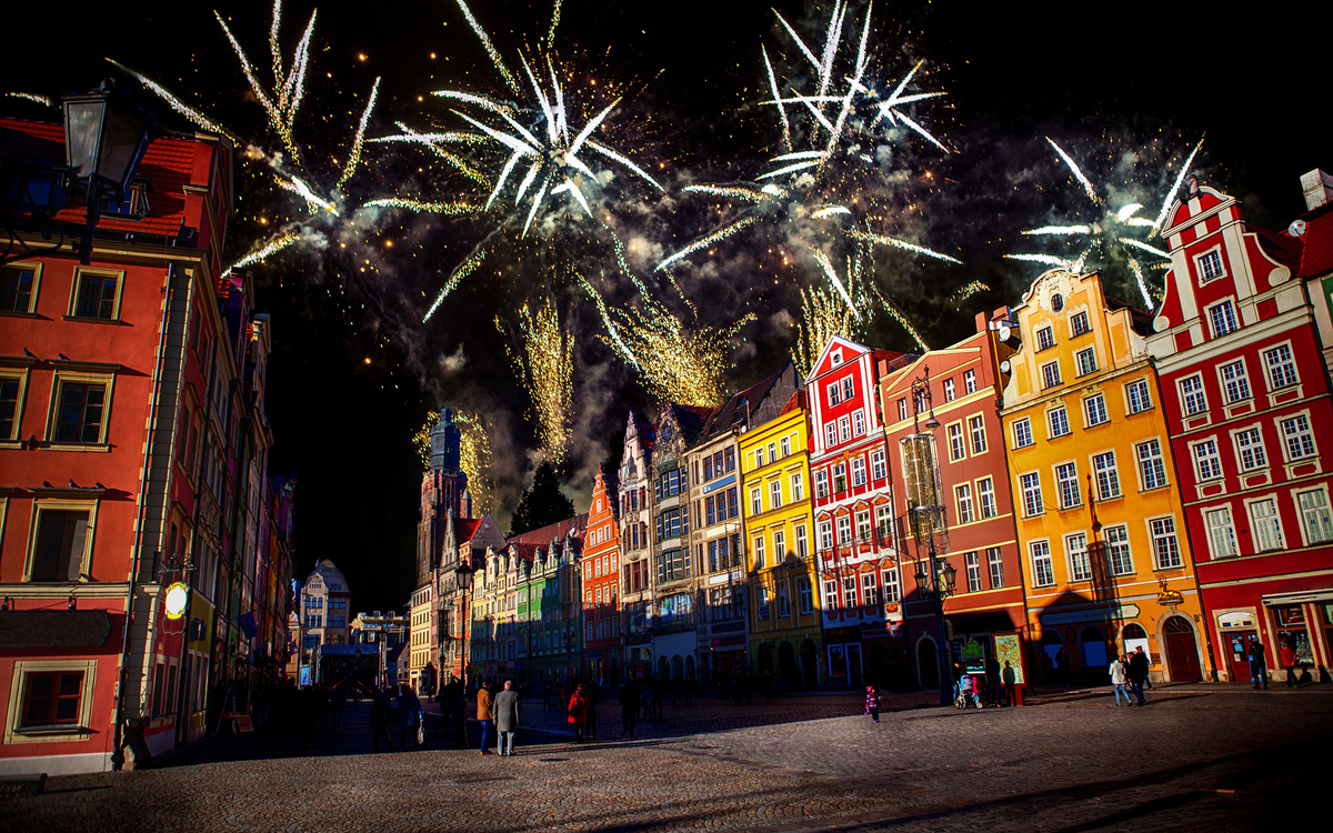 Feuerwerk über einem bunten, historischen Stadtplatz bei Nacht.