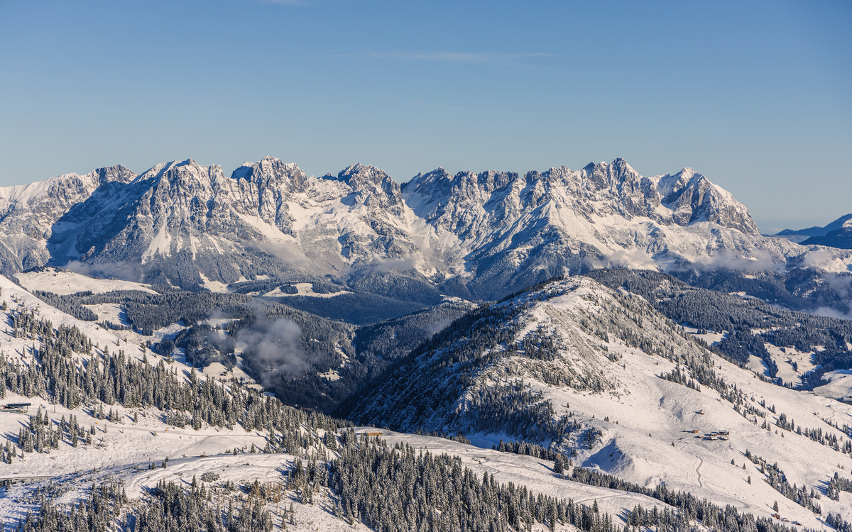 Verschneite Berglandschaft mit klarer Sicht auf das Gebirgsmassiv unter blauem Himmel.