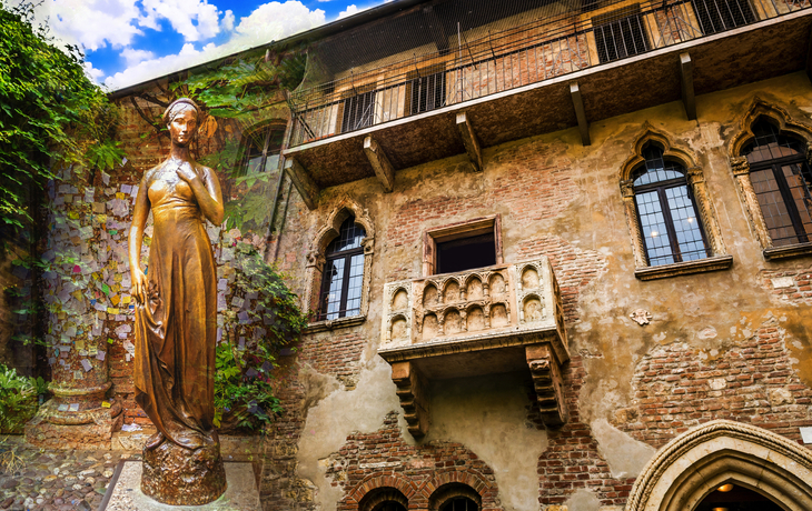 Statue vor einem historischen Backsteingebäude mit Balkon.