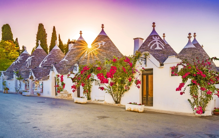 Trulli-Häuser mit Blumen und Sonnenuntergang im Hintergrund