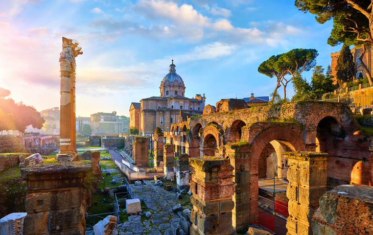 Forum Romanum in Rom bei Sonnenuntergang mit antiken Ruinen und einer Kuppelkirche im Hintergrund.