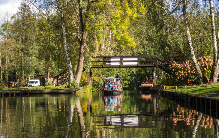 Bootsfahrt auf ruhigem Fluss mit Brücke und Bäumen im Hintergrund