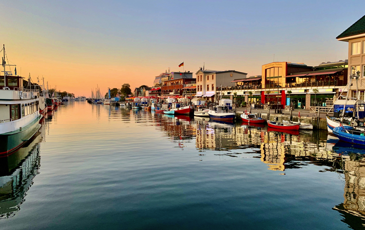 Hafenpromenade bei Sonnenuntergang mit Booten und Gebäuden.