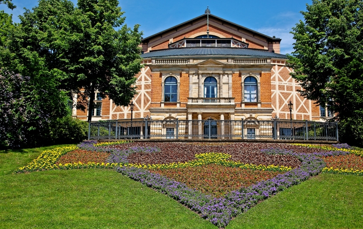 Rotes Backsteingebäude mit Blumenbeeten im Vordergrund und blauem Himmel.