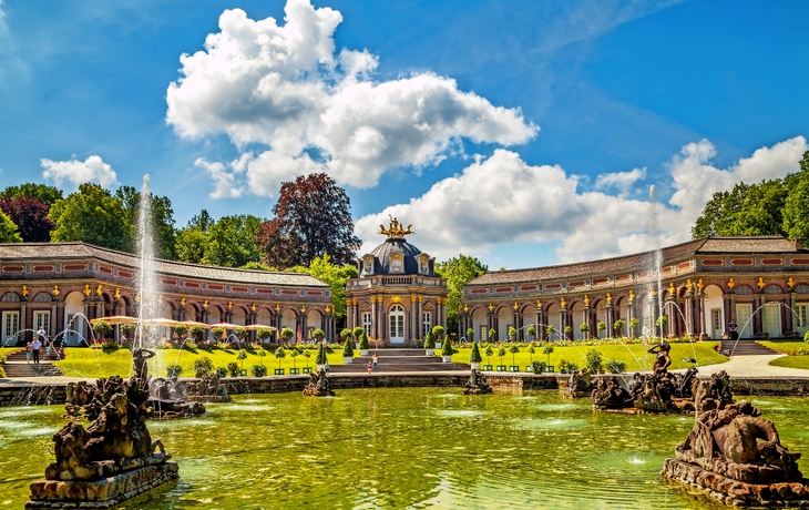 Barockgarten mit Springbrunnen und historischem Gebäude im Hintergrund.