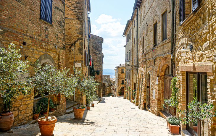 Mittelalterliche, gepflasterte Gasse mit Ziegelsteinhäusern und Blumenkübeln.