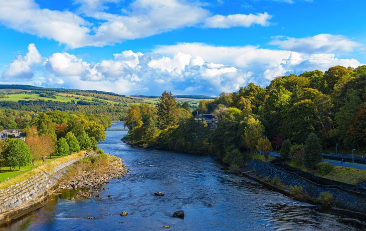 Flusslandschaft mit bewaldeten Ufern und blauem Himmel.