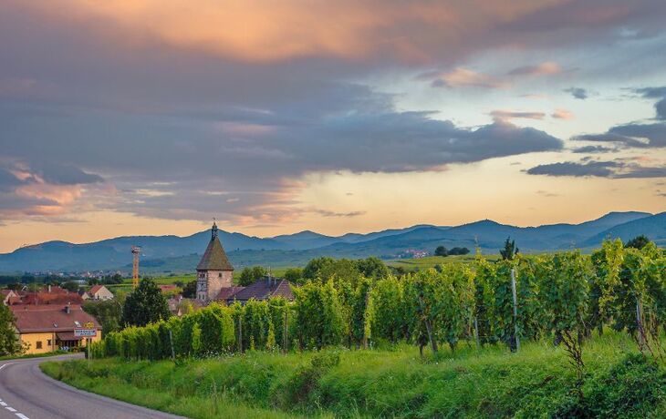 Landschaft mit Weinbergen, Dorf und Bergen im Hintergrund bei Sonnenuntergang.