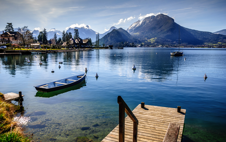 Holzsteg am See mit Bergkulisse und Ruderboot im Wasser