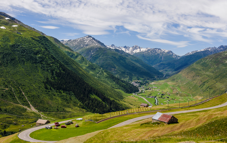 Berglandschaft mit grünen Tälern und schneebedeckten Gipfeln im Hintergrund.