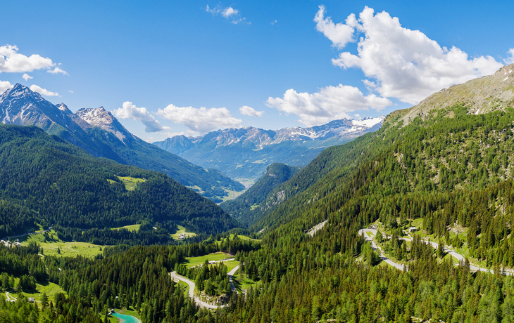 Panoramablick auf bergige Landschaft mit Wäldern und klarem Himmel.