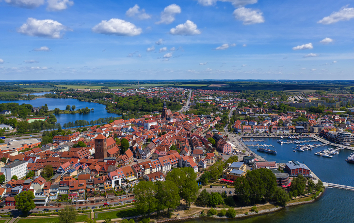 Luftaufnahme einer Stadt mit Hafen, rotem Ziegeldach und umgebender Landschaft.