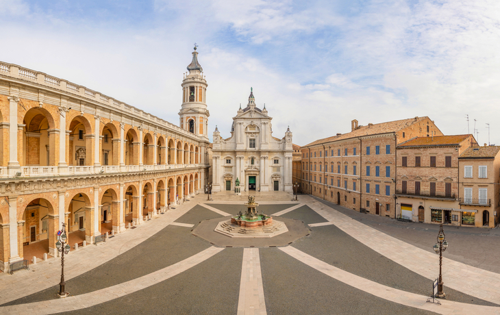 Historischer Platz mit Kolonnaden, Kirche und Springbrunnen an einem sonnigen Tag