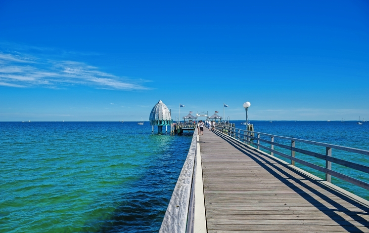 Steg führt auf die Ostsee mit gläserner Kuppel im Hintergrund.